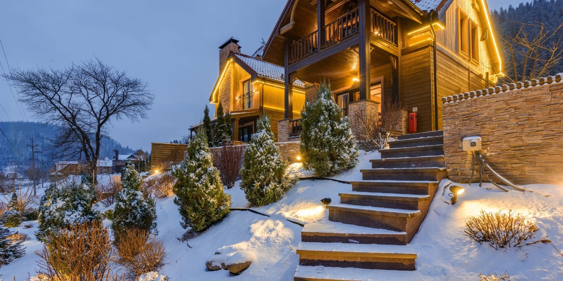Wooden cabin in a snowy landscape with illuminated steps and lights.