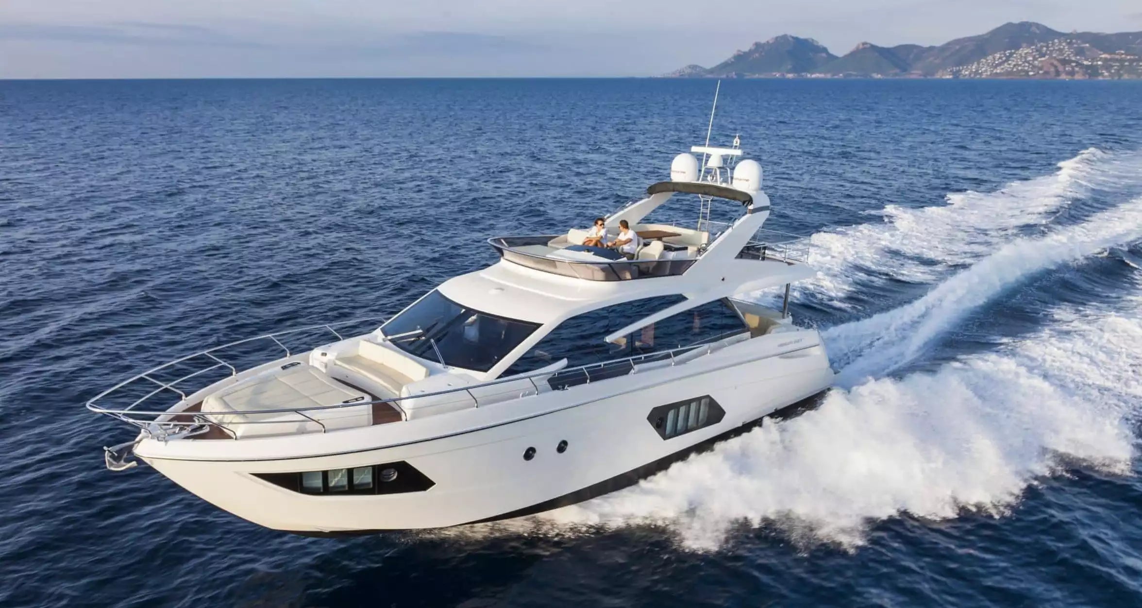 White yacht speeding on the ocean with mountains in the background
