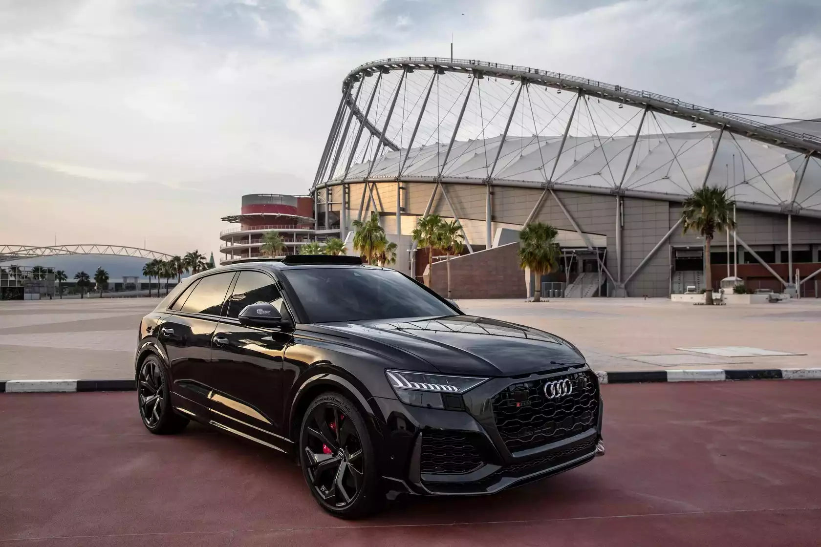 Black Audi SUV parked in front of a modern building with a stadium-like structure.