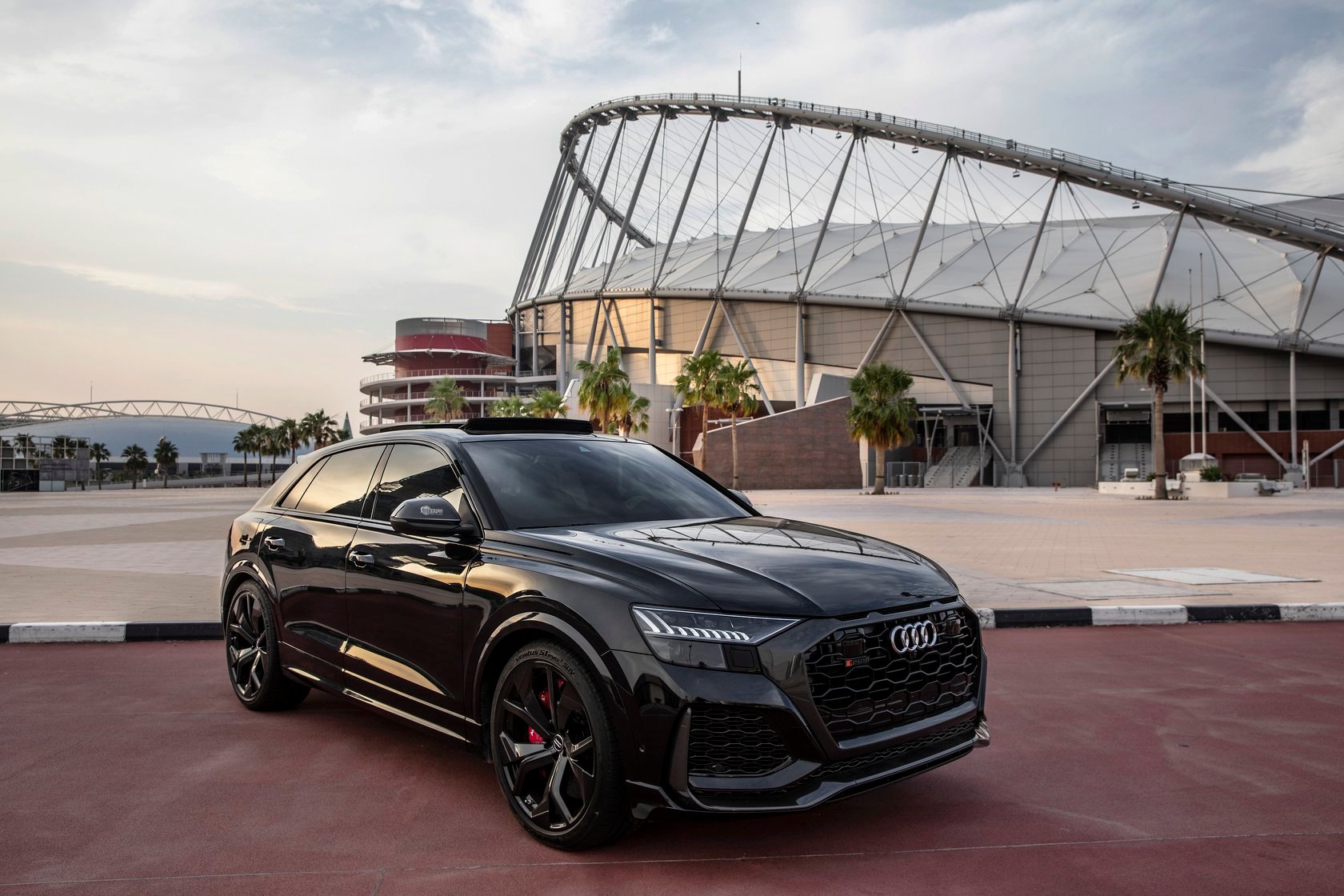 Black Audi SUV parked in front of a modern building with a stadium-like structure.
