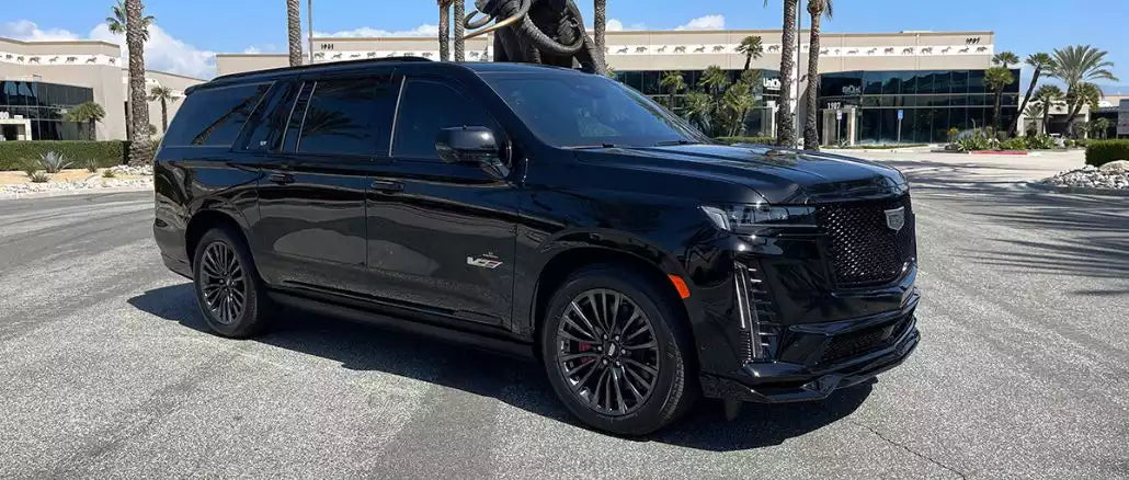 Black SUV parked on a street with palm trees and buildings in the background