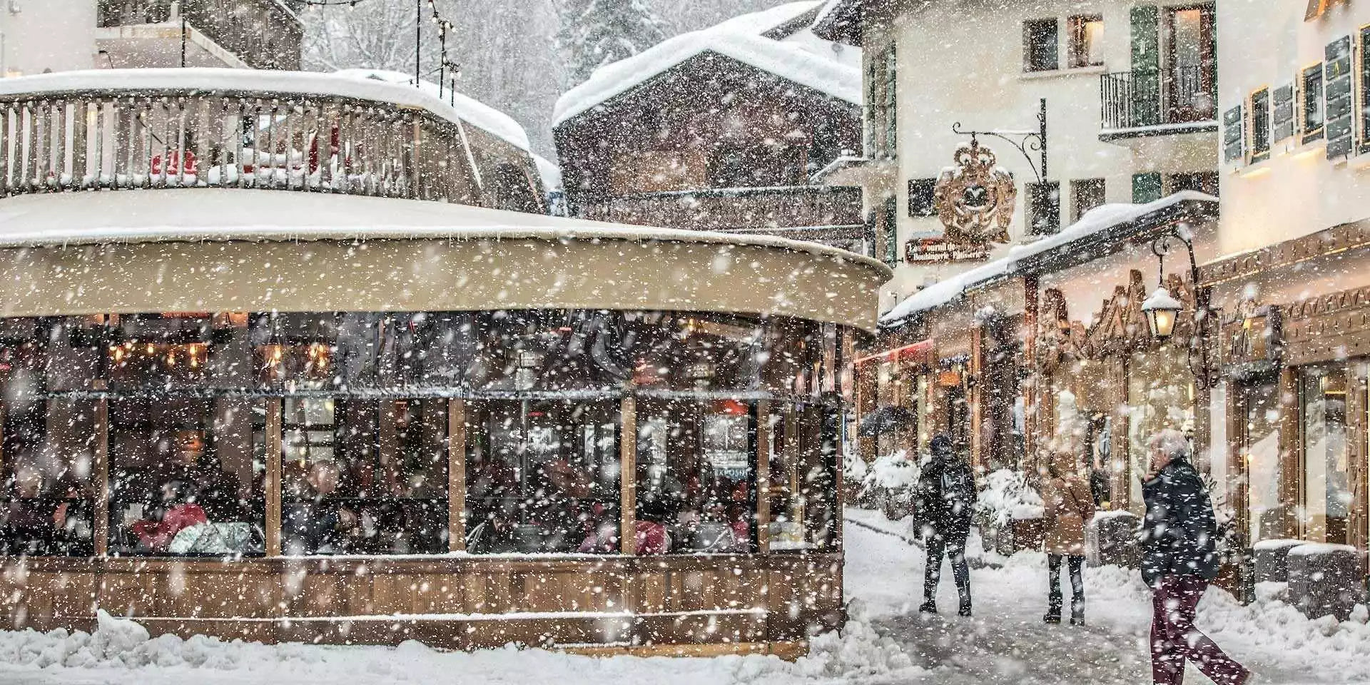 Snowy street scene with a tram and people walking in a town during a snowfall.