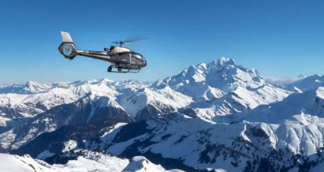 Helicopter flying over snow-covered mountains on a clear day