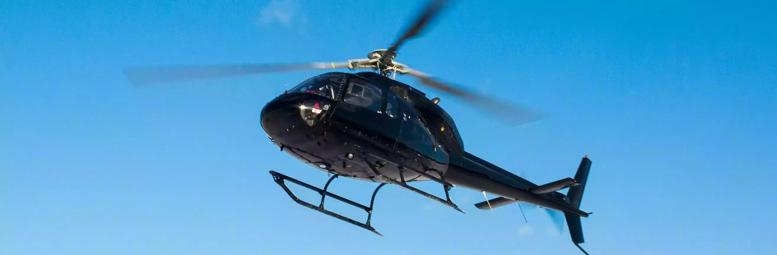 Black helicopter flying against a clear blue sky