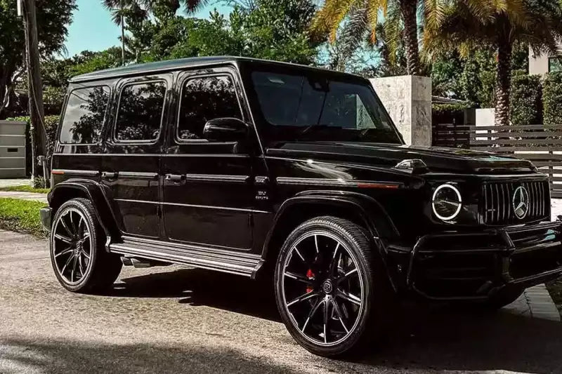 Black Mercedes-Benz G-Class SUV parked on a driveway with palm trees in the background