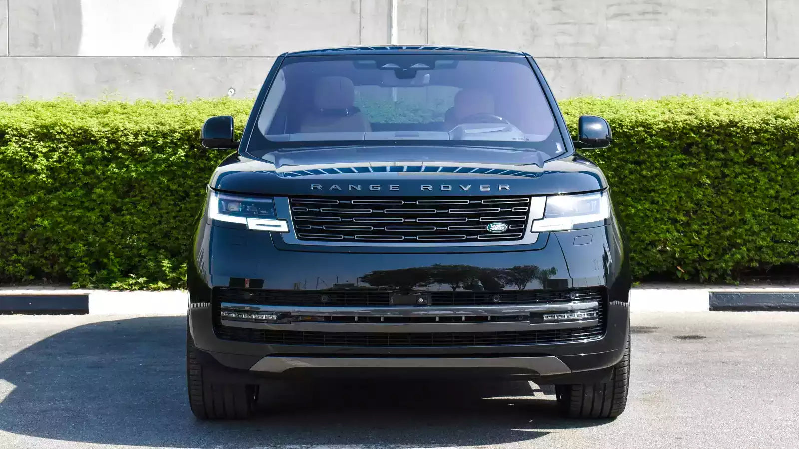 Black Range Rover parked on a street with green bushes in the background