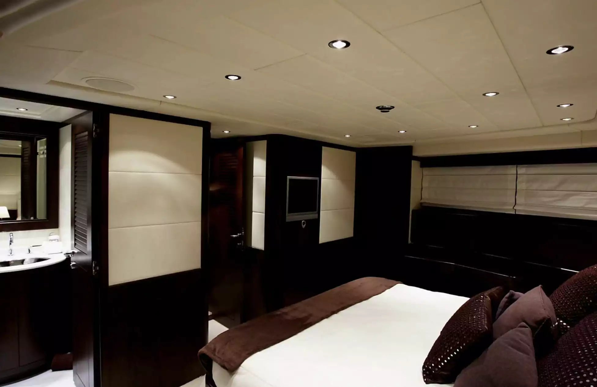 Luxury interior of a yacht cabin with bed, television, and wood paneling.