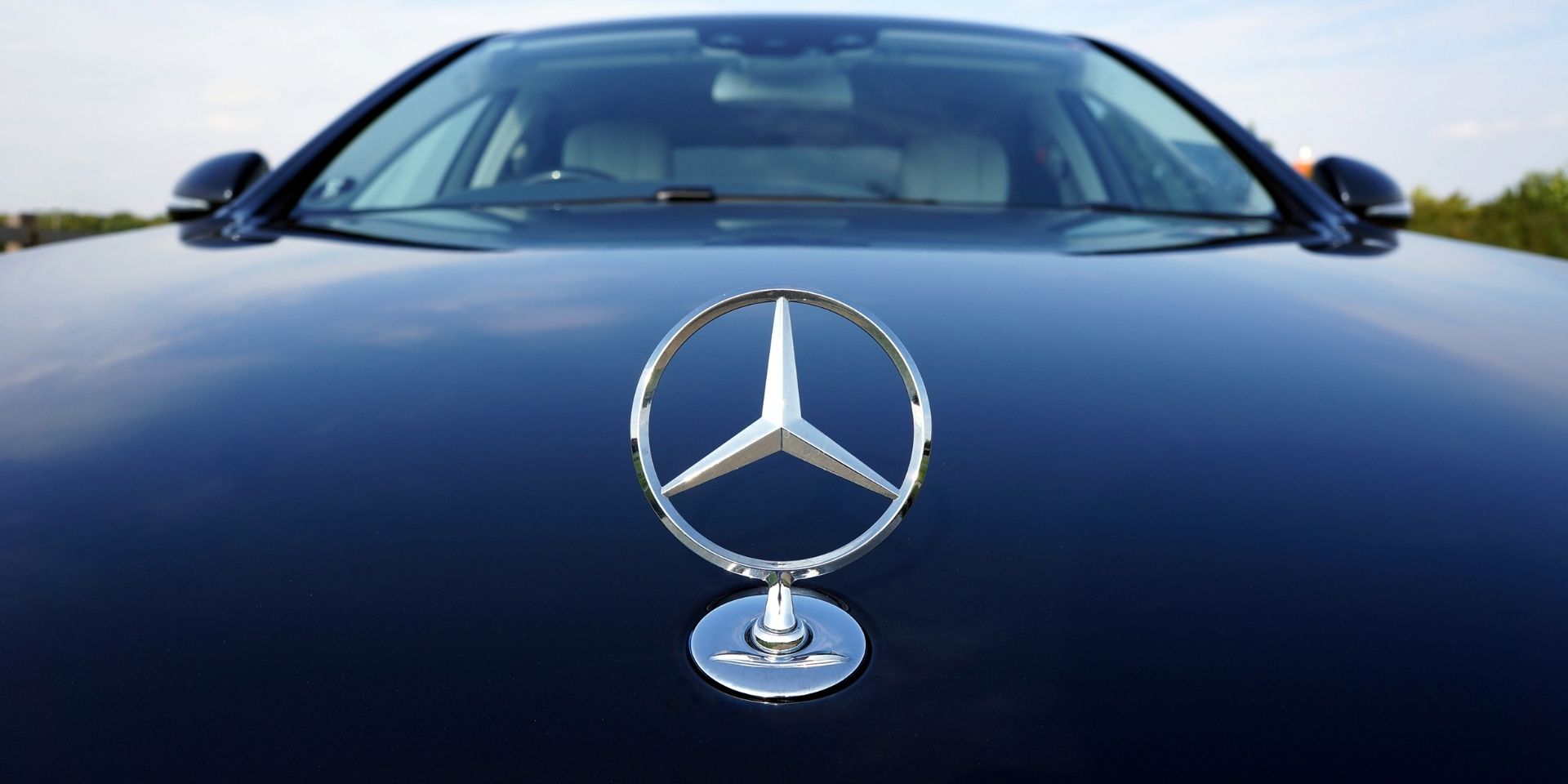 Mercedes-Benz logo on a car hood with a clear sky background