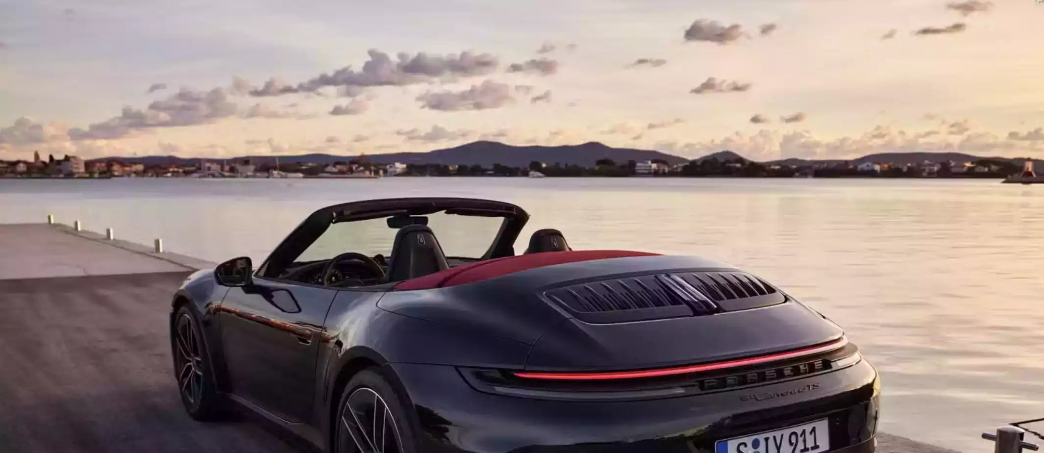 Black Porsche convertible driving on a road by a waterfront with a scenic background