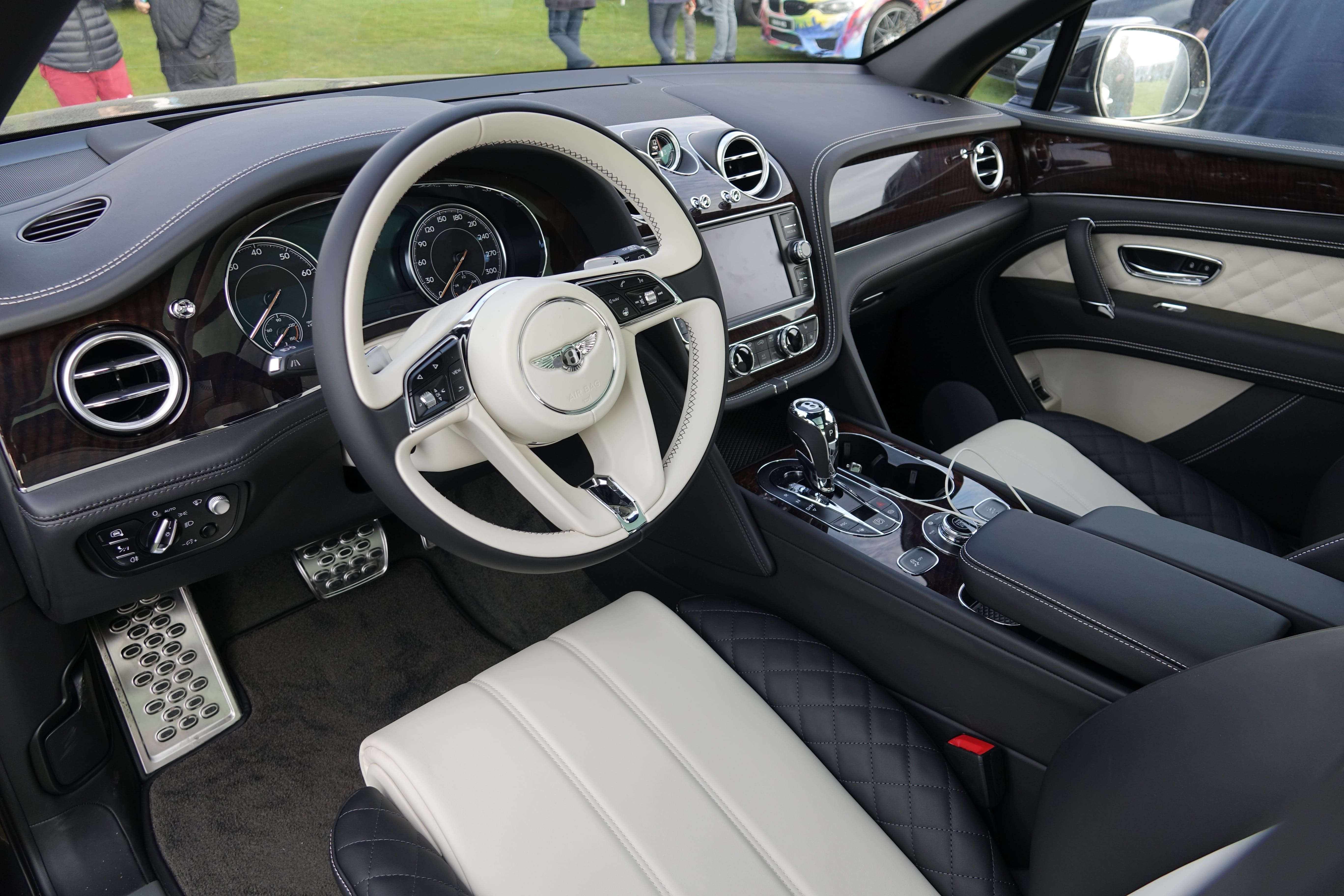 Luxury car interior with cream and black leather seats, dark wood trim, a multi-function steering wheel with a central logo, and a center console with a gear shifter.