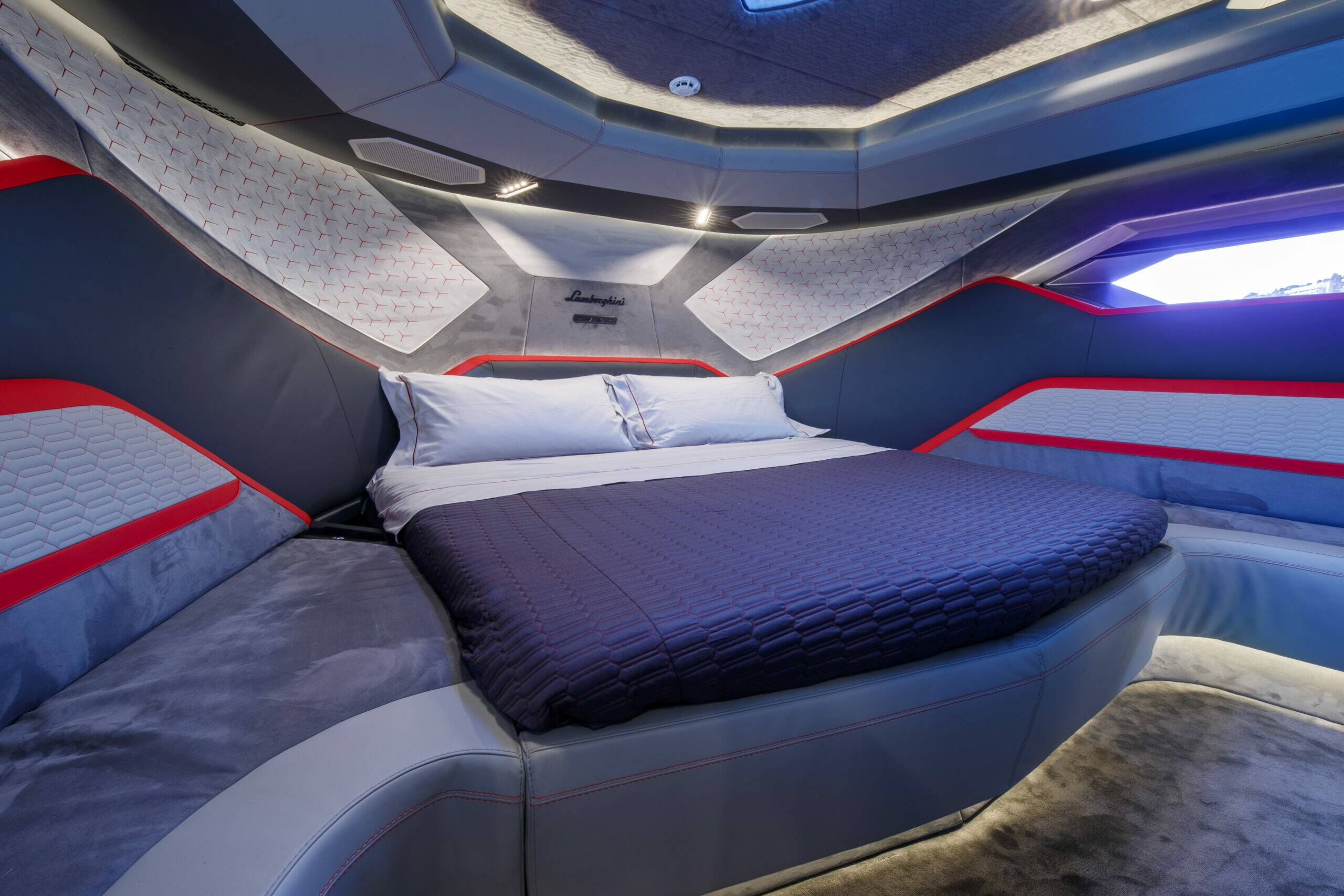 A futuristic capsule-style bed with a curved gray and white frame, red accent lines, a dark quilted bedding cover, and white pillows, photographed in a high-tech interior with blue ambient lighting.