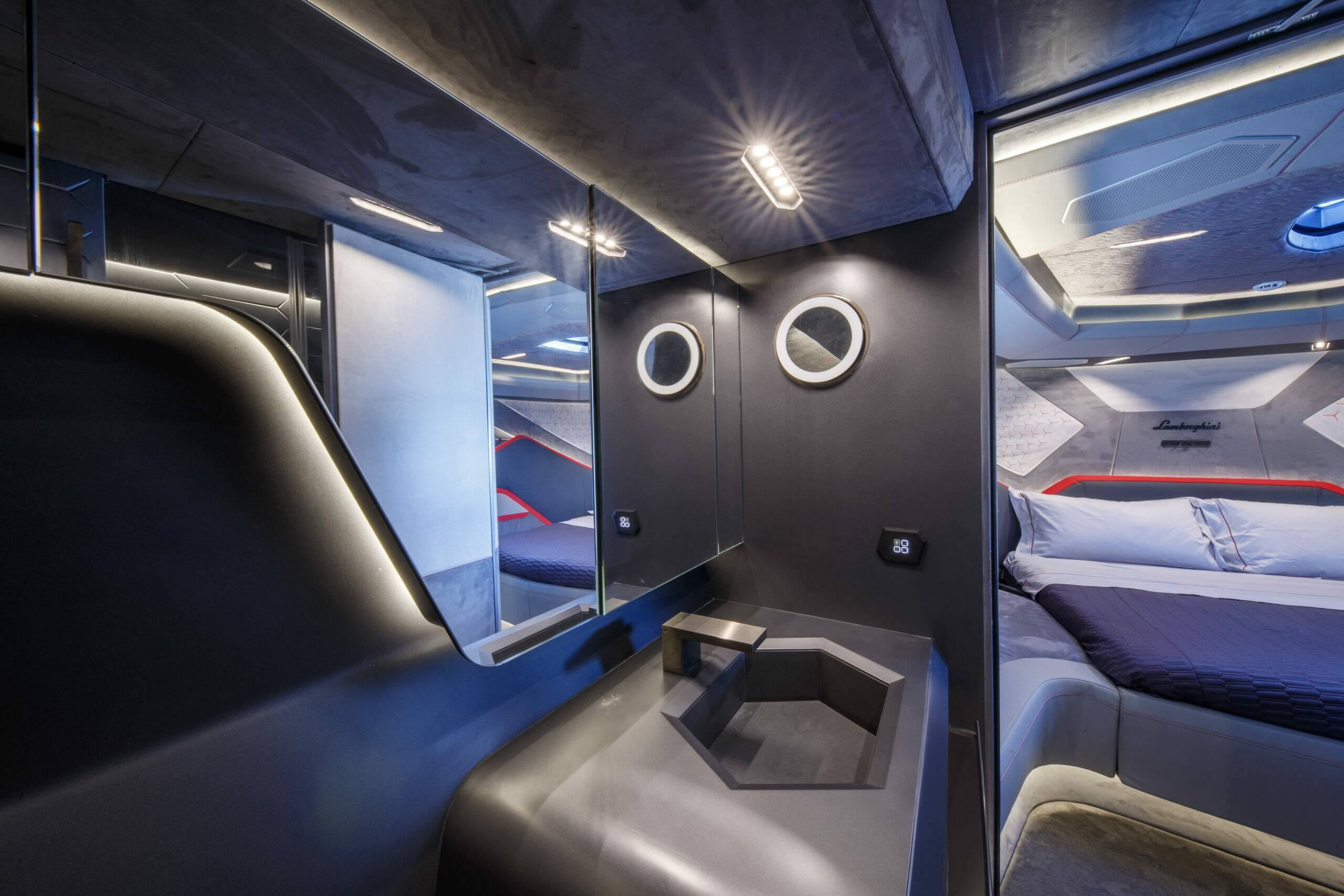 A futuristic compact camper interior with a gray vanity, circular porthole windows, and a bed visible through an adjacent doorway, lit by integrated LED lighting.