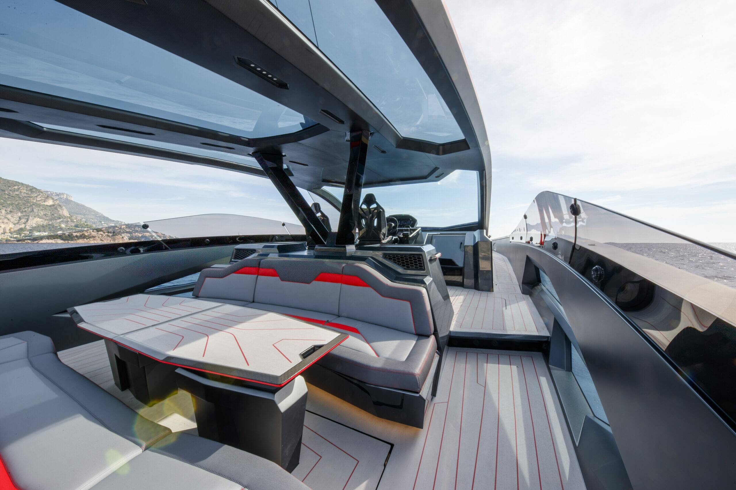 A luxury yacht interior featuring a modern dining area with gray and white upholstered seating, a matching table, and a sleek dark gray cabin structure under a glass canopy.