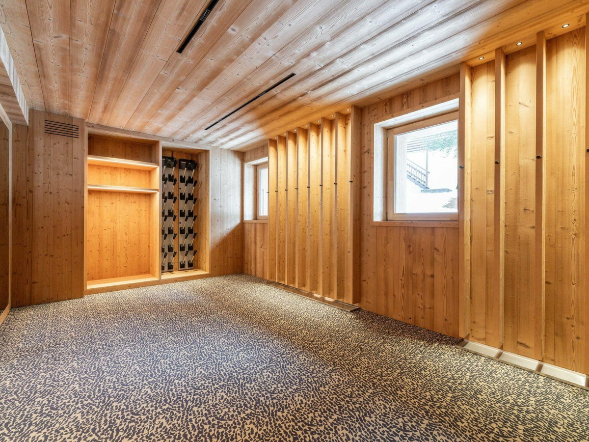 A spacious room with light wood paneled walls and ceiling, a patterned carpeted floor, and built-in shelving and wine racks along one wall.