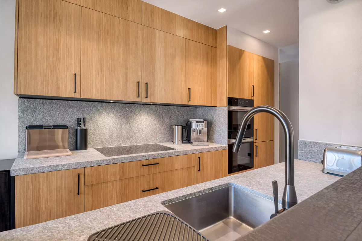 Modern kitchen cabinetry with light wood upper and lower cabinets, speckled gray countertops, a stainless steel sink, and a tall curved faucet.