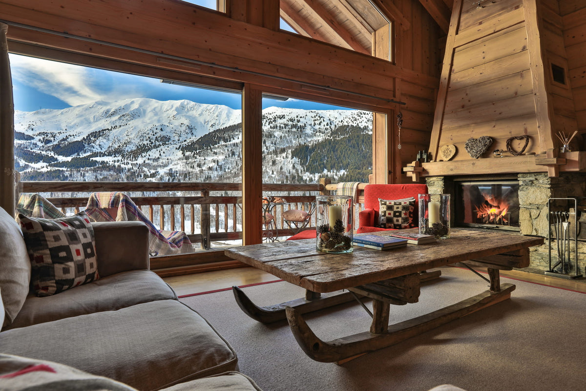 A rustic wooden ski lift coffee table in a cozy alpine chalet living room, set against a large window with a snowy mountain landscape view.