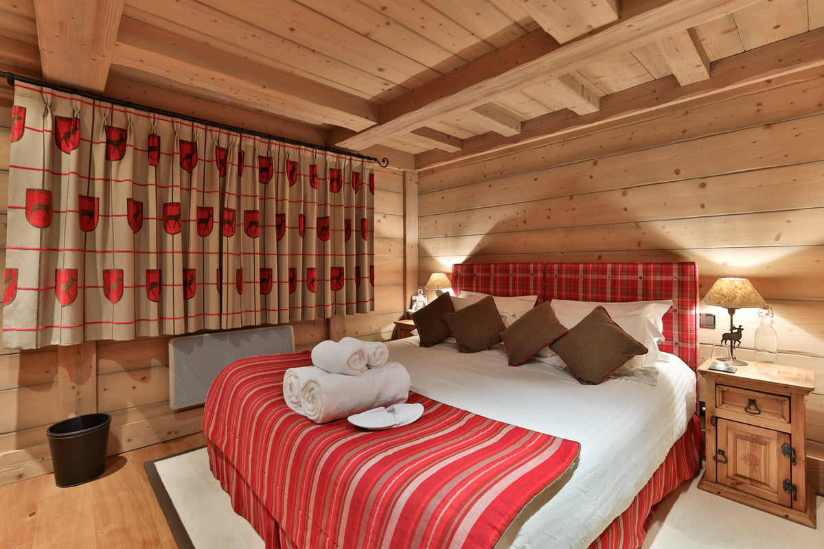 A cozy bedroom with a bed dressed in red and white striped bedding, brown pillows, and a red plaid headboard, set in a rustic wood-paneled room with matching patterned curtains.
