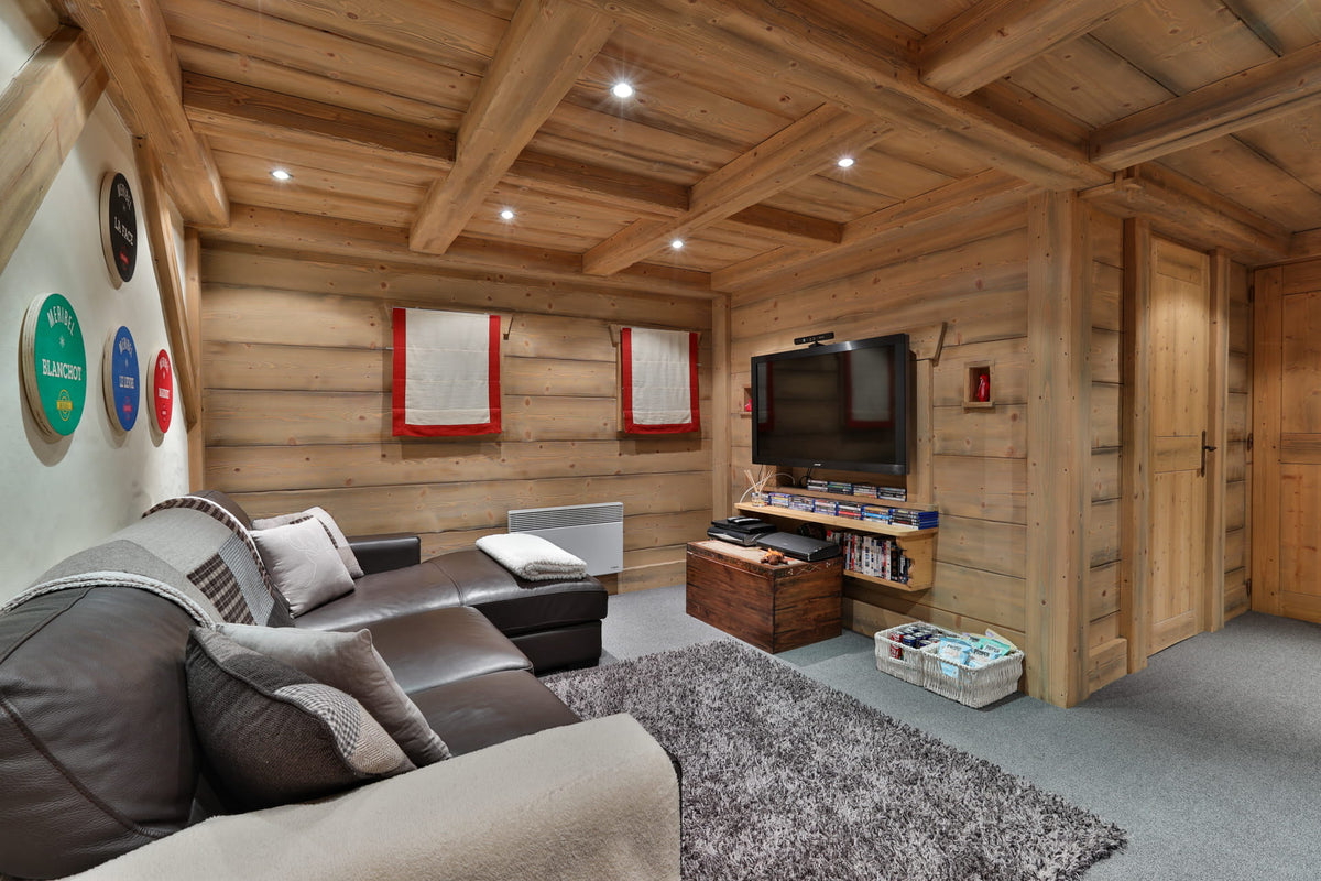 A modern rustic living room with light wood paneled walls and ceiling, featuring a dark brown leather sectional sofa, a gray shag rug, a wall-mounted TV, and decorative circular wall art.