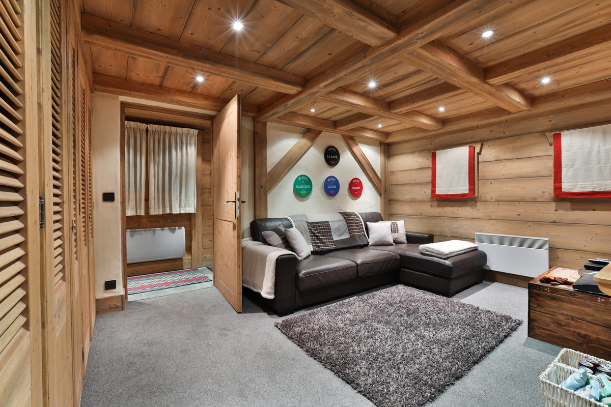 A modern alpine-style living room with a dark brown leather sectional sofa, a gray shag rug, and warm wood-paneled walls and ceiling with recessed lighting.