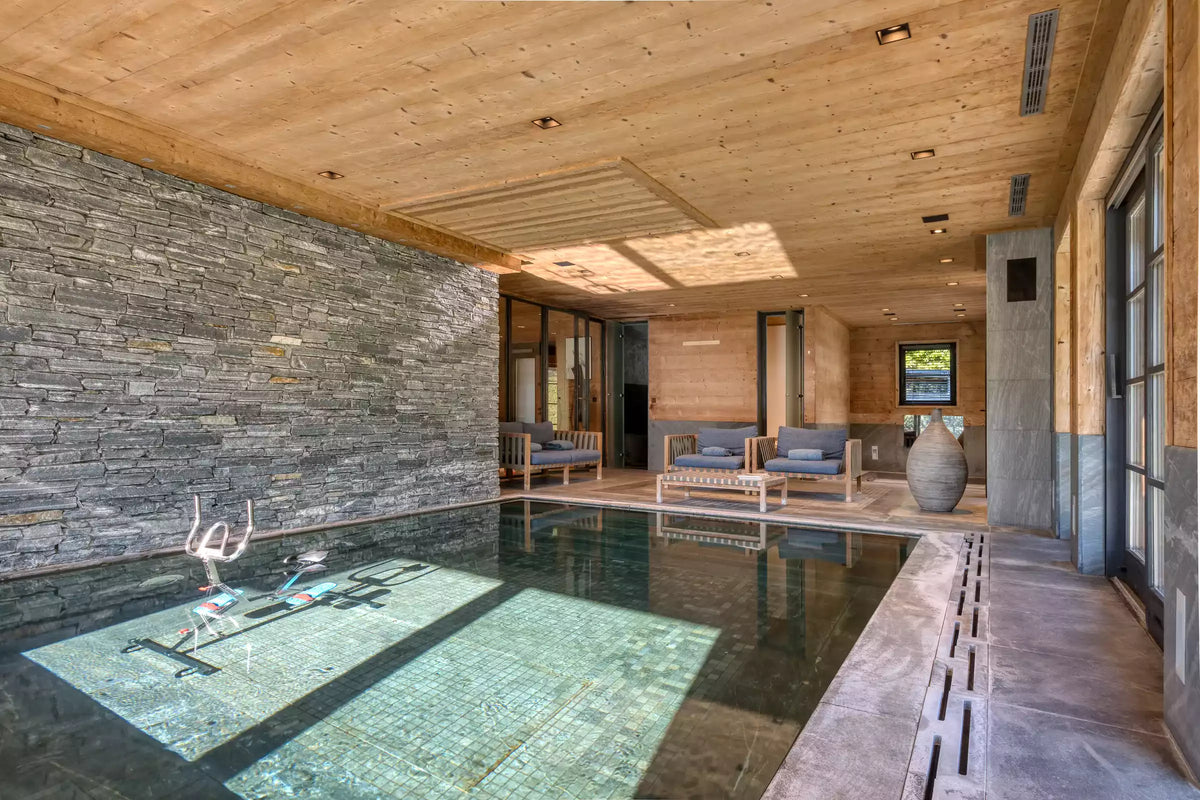 An indoor resort-style pool area with a large stone wall on one side, wood ceiling panels, and seating along the poolside. No person or animal is present, and the scene appears to be a real environment rather than a studio product shot, so this fits Lifestyle rather than Product/Packaging.