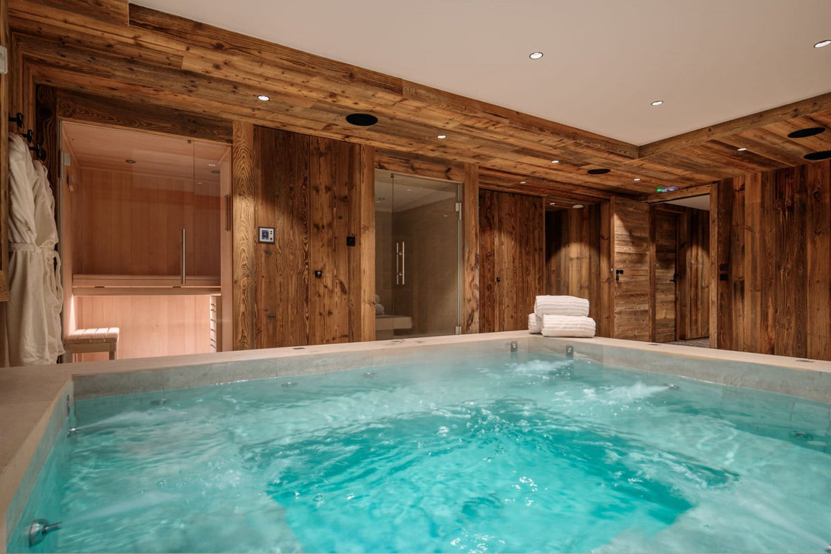 An indoor hot spring or bubbling pool with bright turquoise water, surrounded by rustic wood-paneled walls and ceiling, with a sauna and other rooms visible in the background.