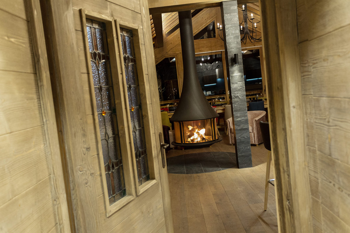 A modern black cone-shaped fireplace with a visible fire, situated in a rustic wooden lodge interior with light wood paneled walls and doors.