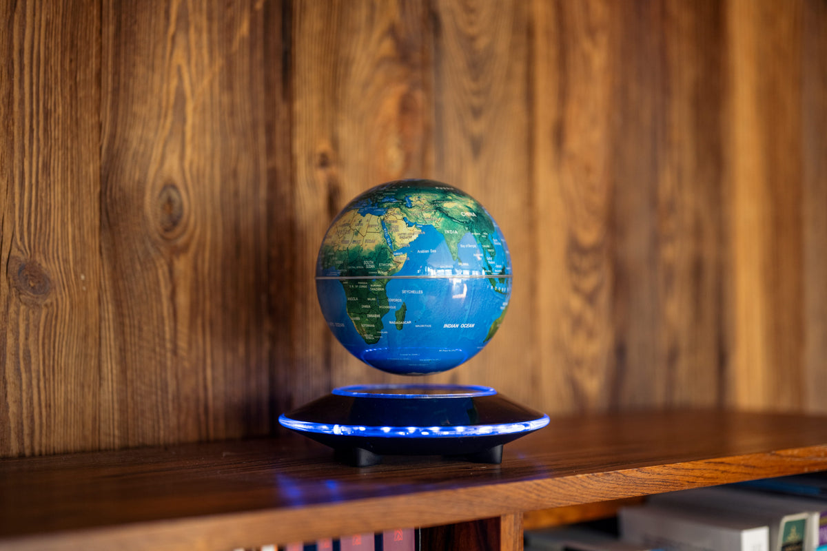 A floating globe model resting on a circular magnetic base, placed on a wooden shelf against a wooden wall background.