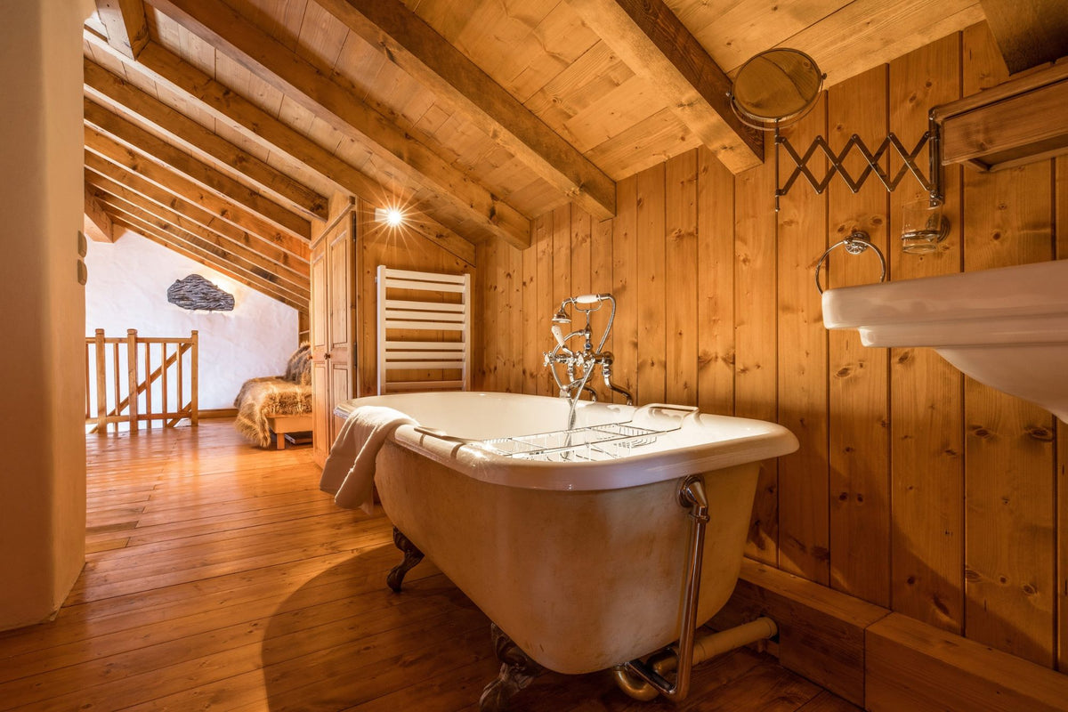 A vintage-style white clawfoot bathtub with chrome plumbing installed in a rustic wooden bathroom with exposed wood ceiling beams and wood-paneled walls.