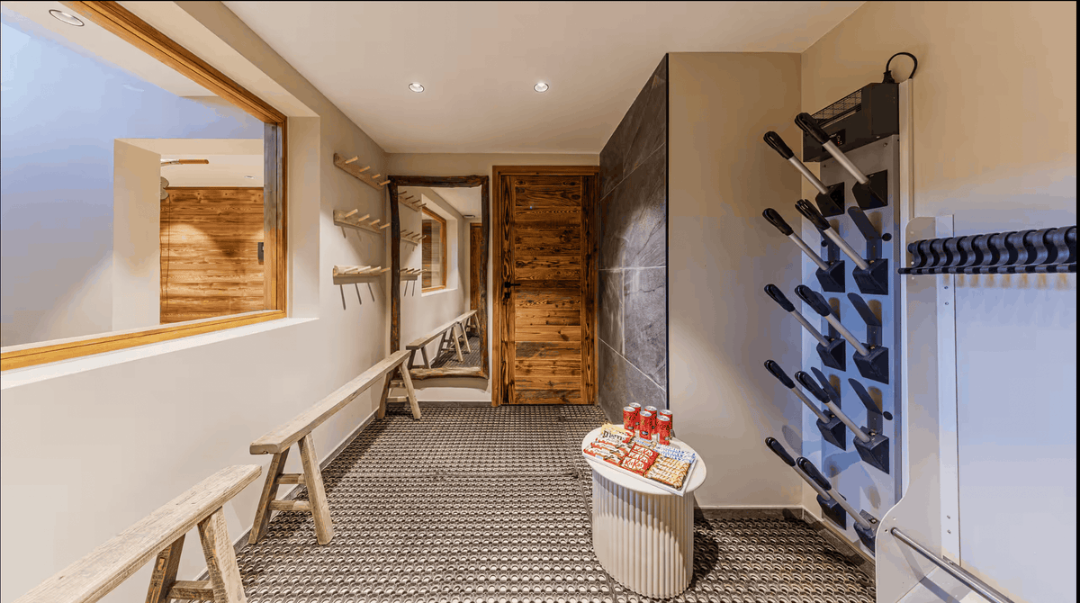 A modern interior hallway or storage space with a black-and-white patterned floor, a wooden door, a large window, wall-mounted racks, and a small round table holding red and white packaged items.