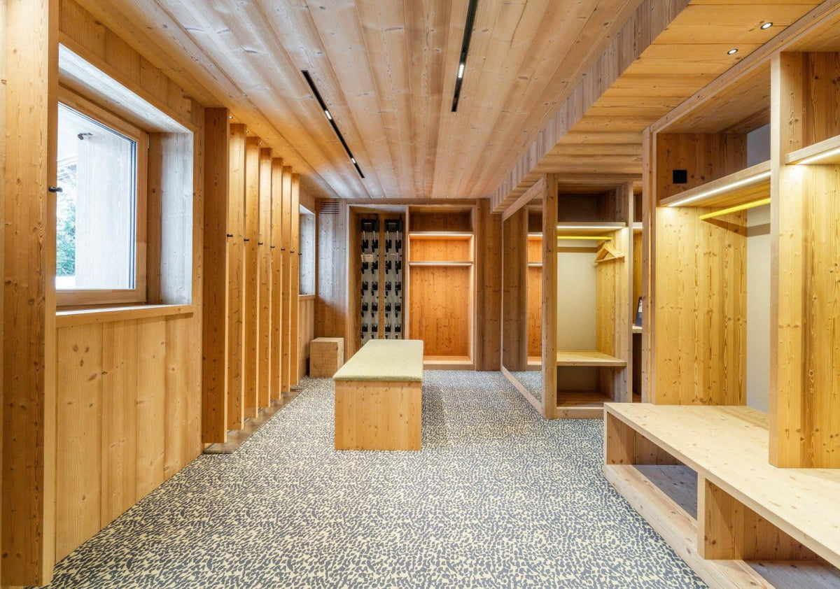 A modern wooden walk-in closet or storage room with light wood paneled walls and ceiling, built-in shelving, a bench, mirror, and a speckled gray floor.