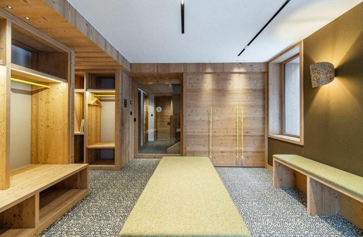 A modern wooden interior space with built-in shelving, benches, a long light-colored rug, textured walls, and a window, shown as a real environment rather than a isolated product shot.