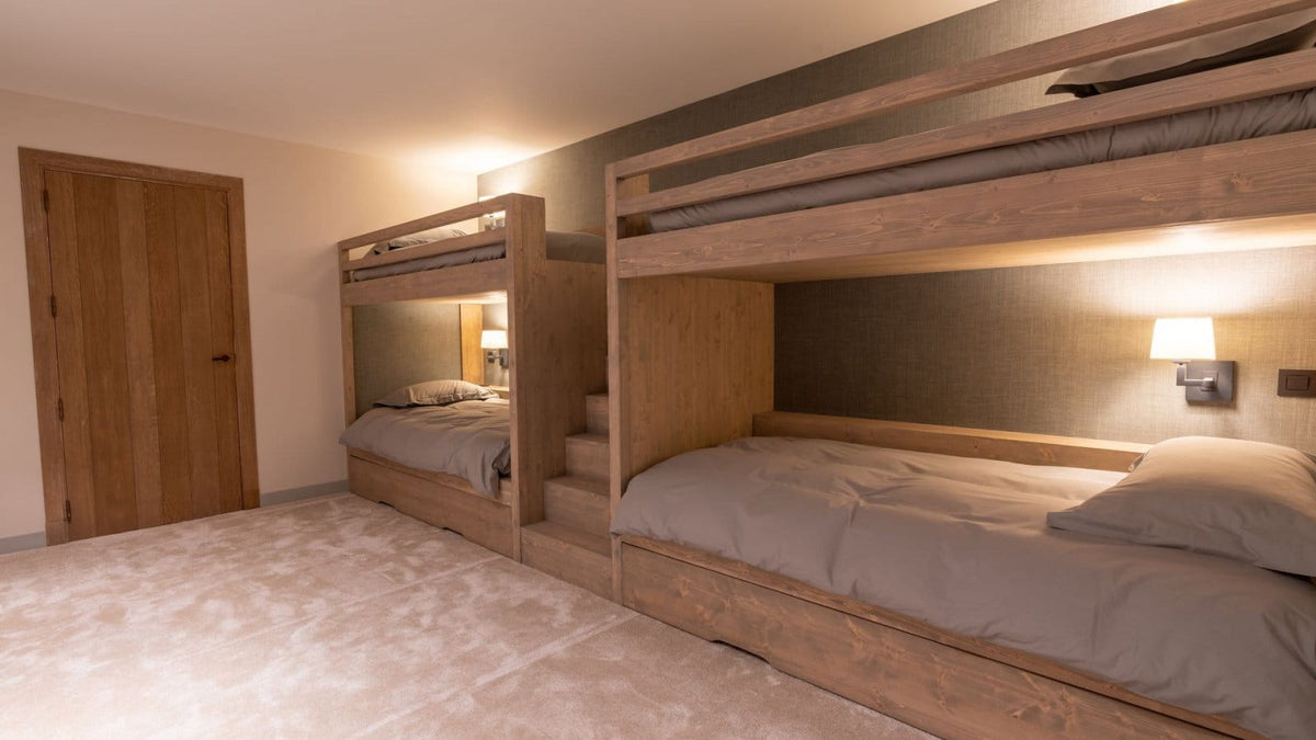 A modern bedroom featuring two wooden bunk beds with light gray bedding, wall-mounted lamps, and a carpeted floor.