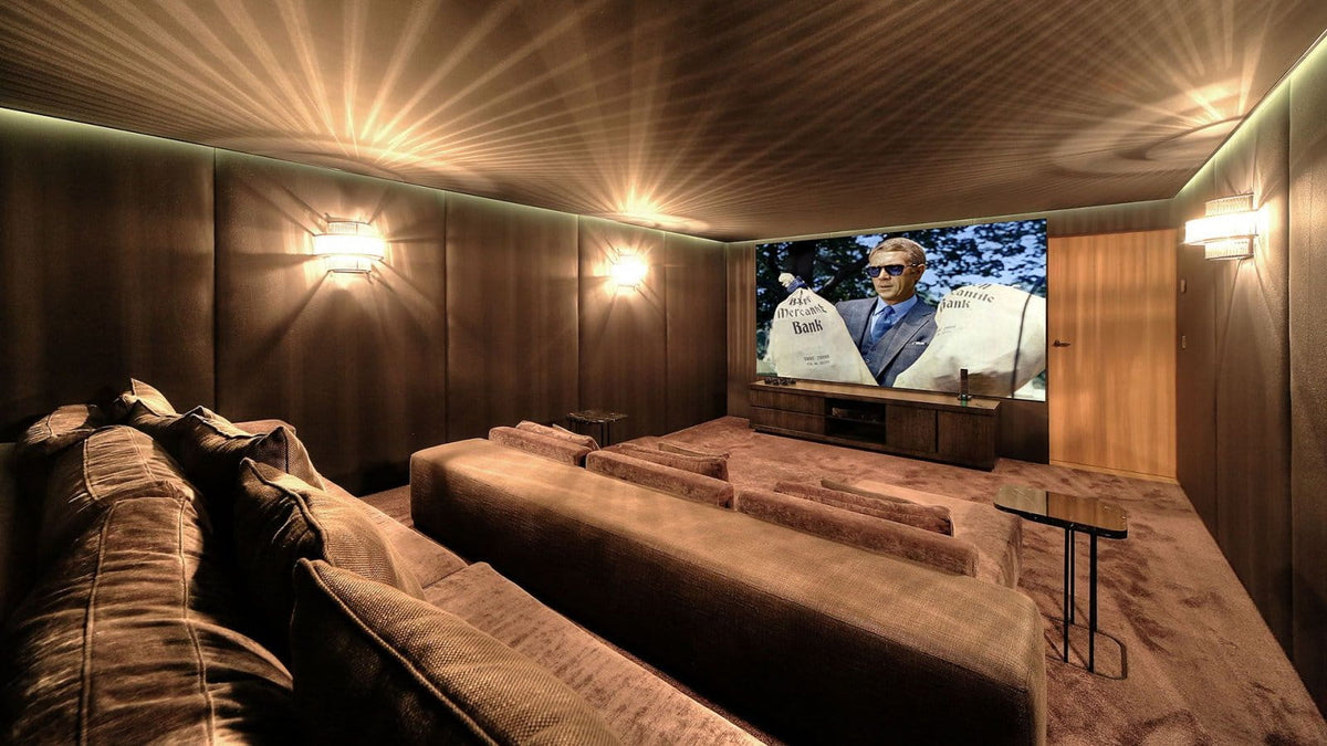A home theater interior with tiered plush theater seating, wood-paneled walls, wall-mounted lights, and a large screen displaying a movie scene.