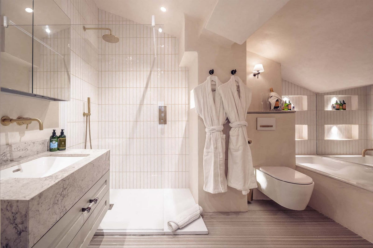 Luxury modern bathroom featuring a walk-in shower with white tiled walls, a marble vanity, a white toilet, a bathtub, and two white bathrobes hanging on the wall.