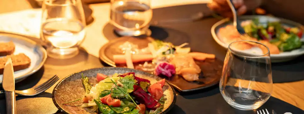 Dinner table with plates of food, glasses, and cutlery on a wooden surface.