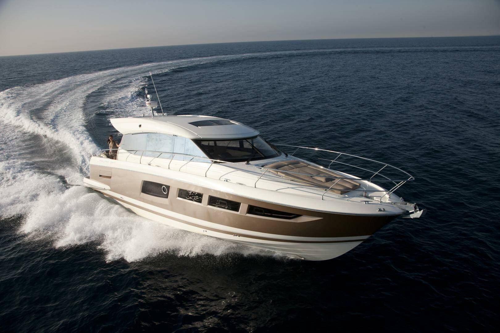 A luxury motor yacht with a white and beige hull speeds across deep blue ocean water, leaving a white wake behind it.