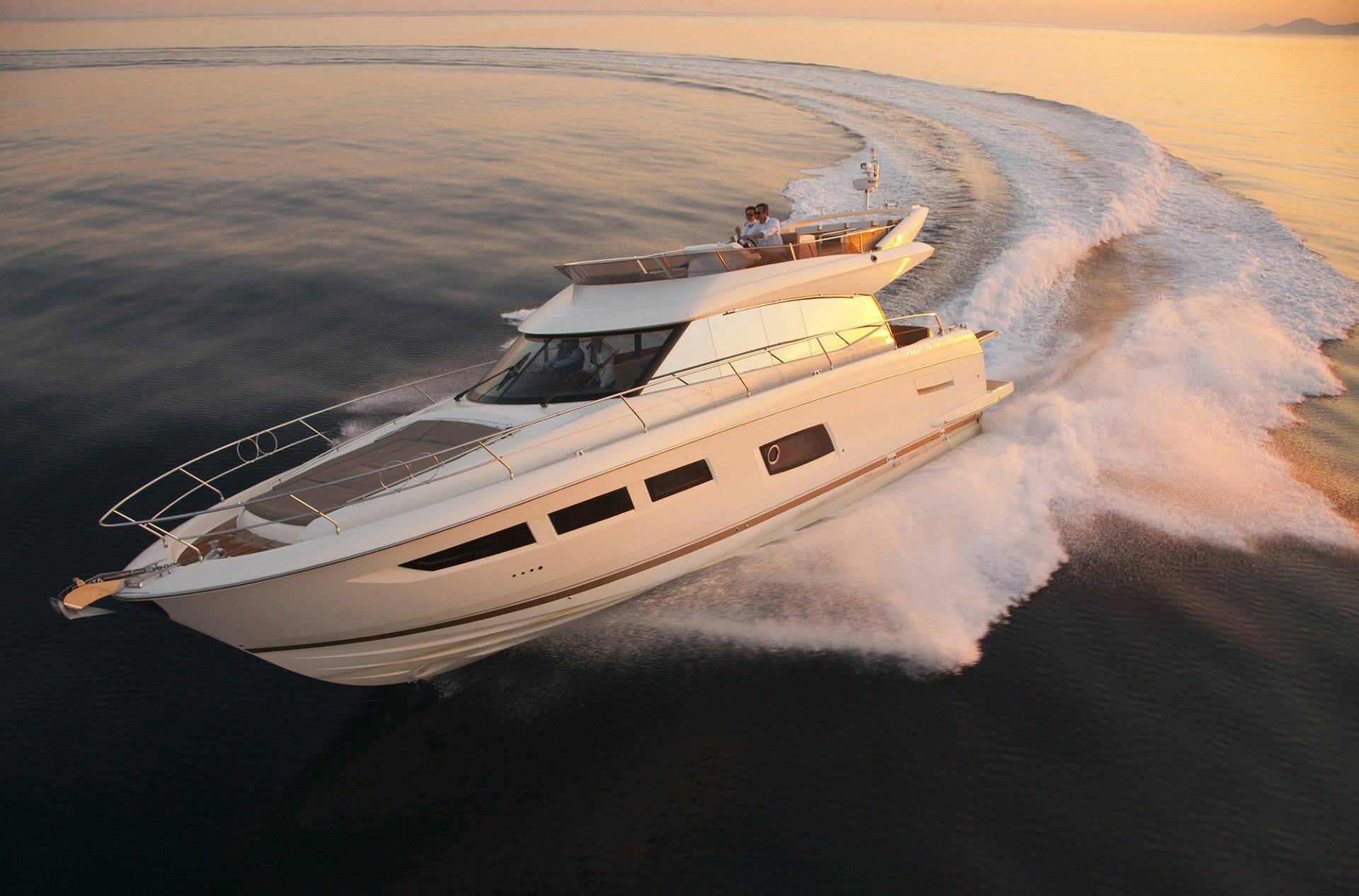 A luxury motor yacht speeds across dark ocean water, creating a large white wake, during golden hour with warm sunlight reflecting off the hull and water.