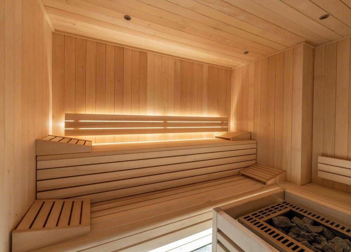 A warm, inviting wooden sauna interior with tiered seating, backlit shelves, and a stone firebox in the foreground.