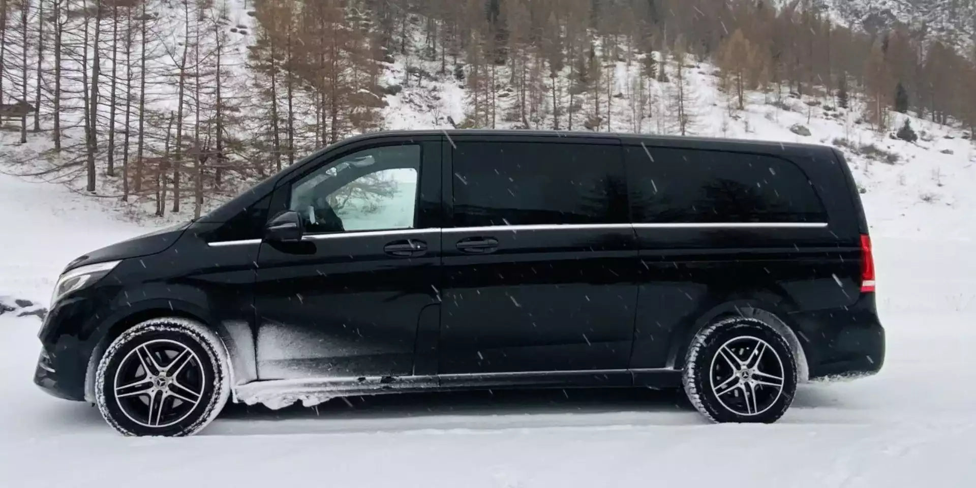Black van on a snowy landscape with trees in the background