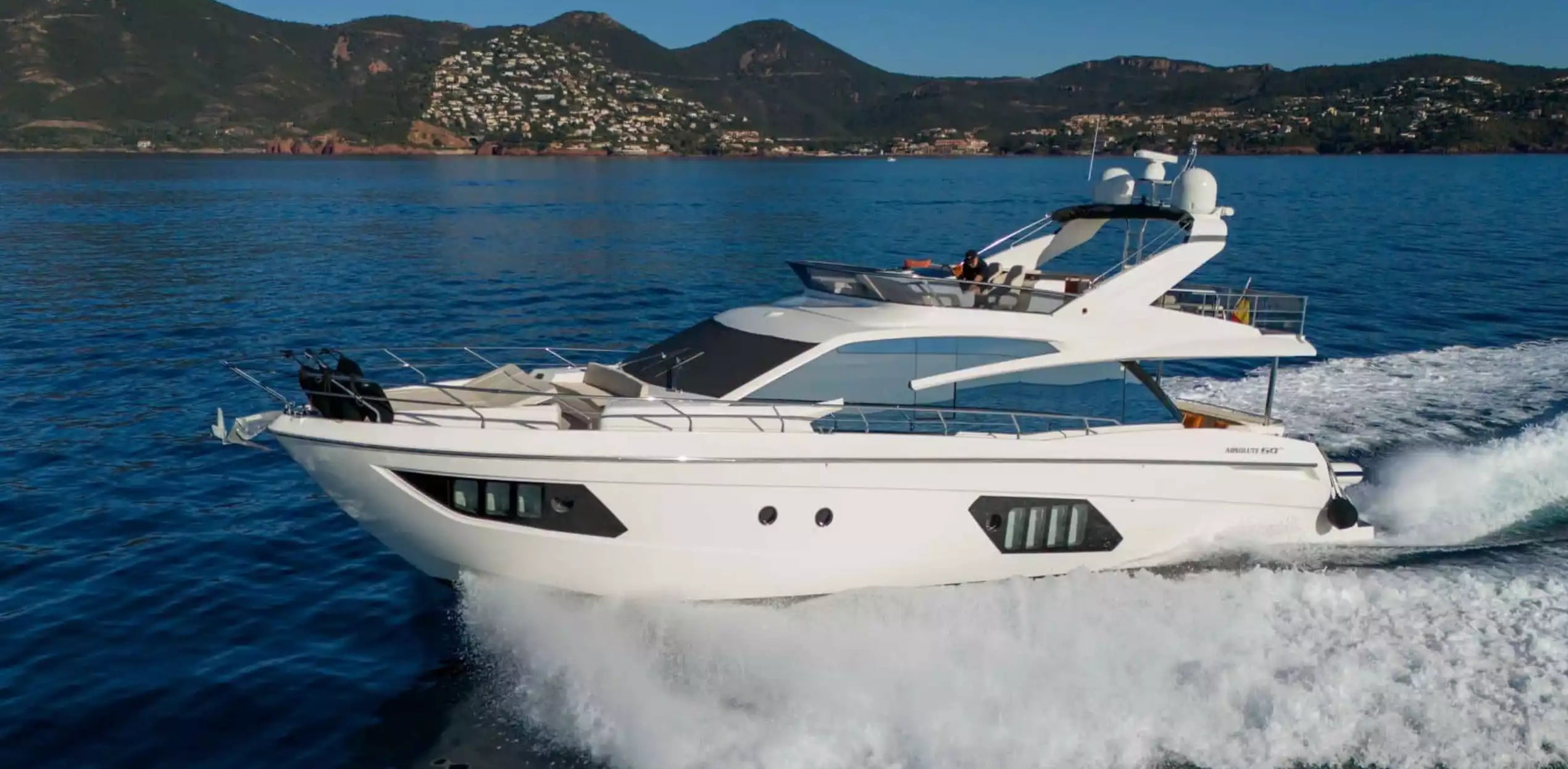 White yacht speeding on a blue sea with mountains in the background