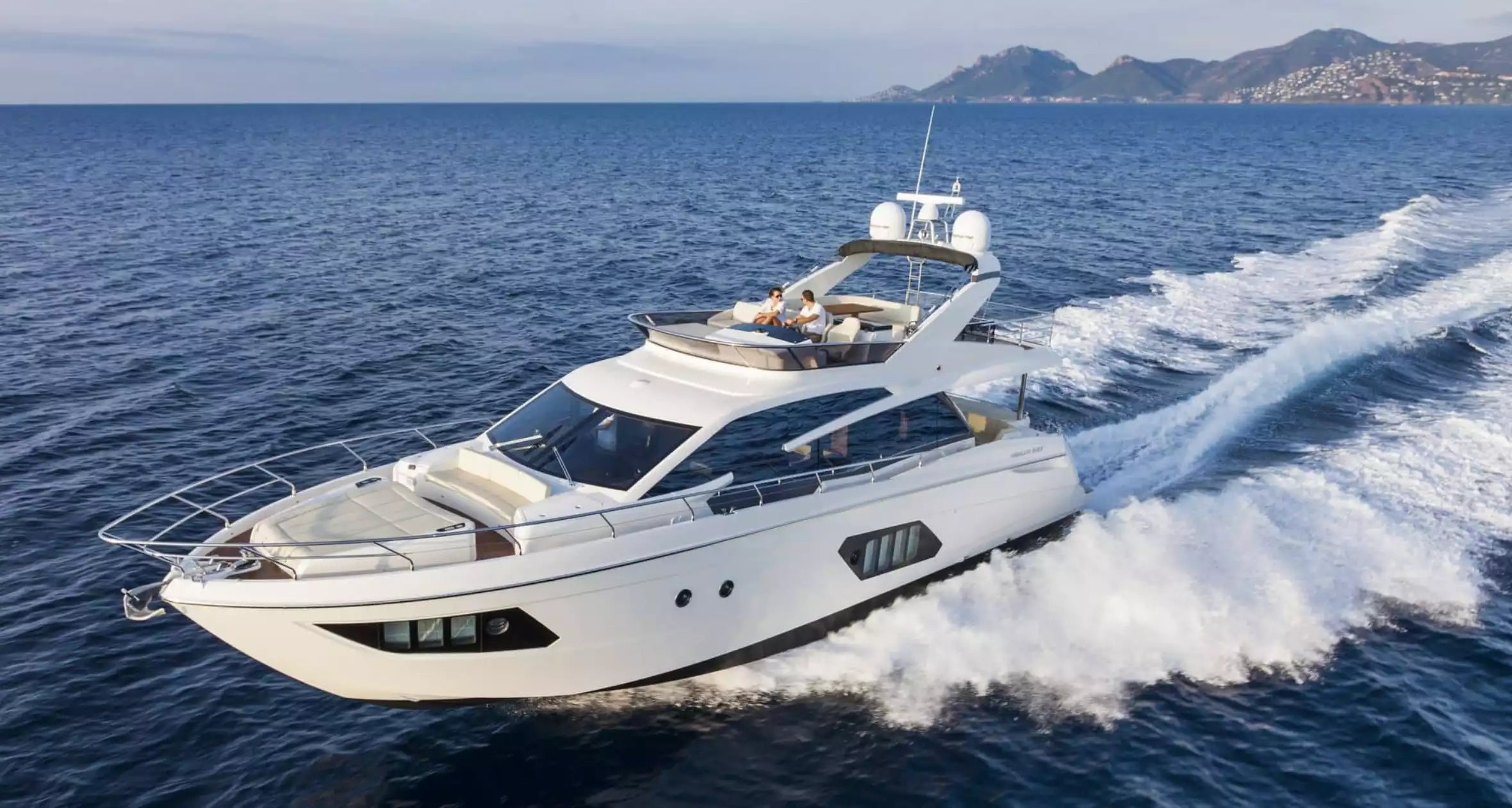 White yacht speeding on the ocean with mountains in the background