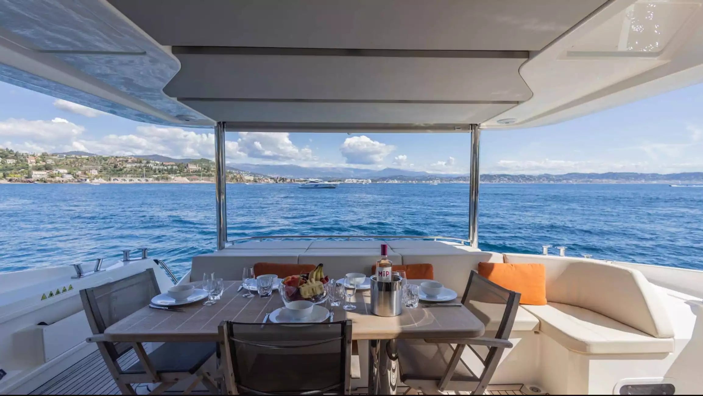 Yacht deck with dining table set for two, overlooking water and coastline.