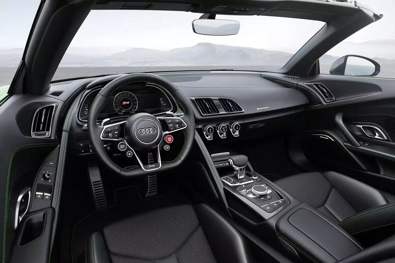 A luxury car interior with a black leather dashboard, steering wheel, and seats, featuring the Audi logo on the center console and green accent stitching.
