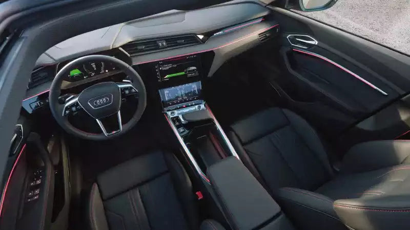 A luxury car interior with black leather seats, a multi-screen display on the dashboard, and red accent stitching and trim lines.