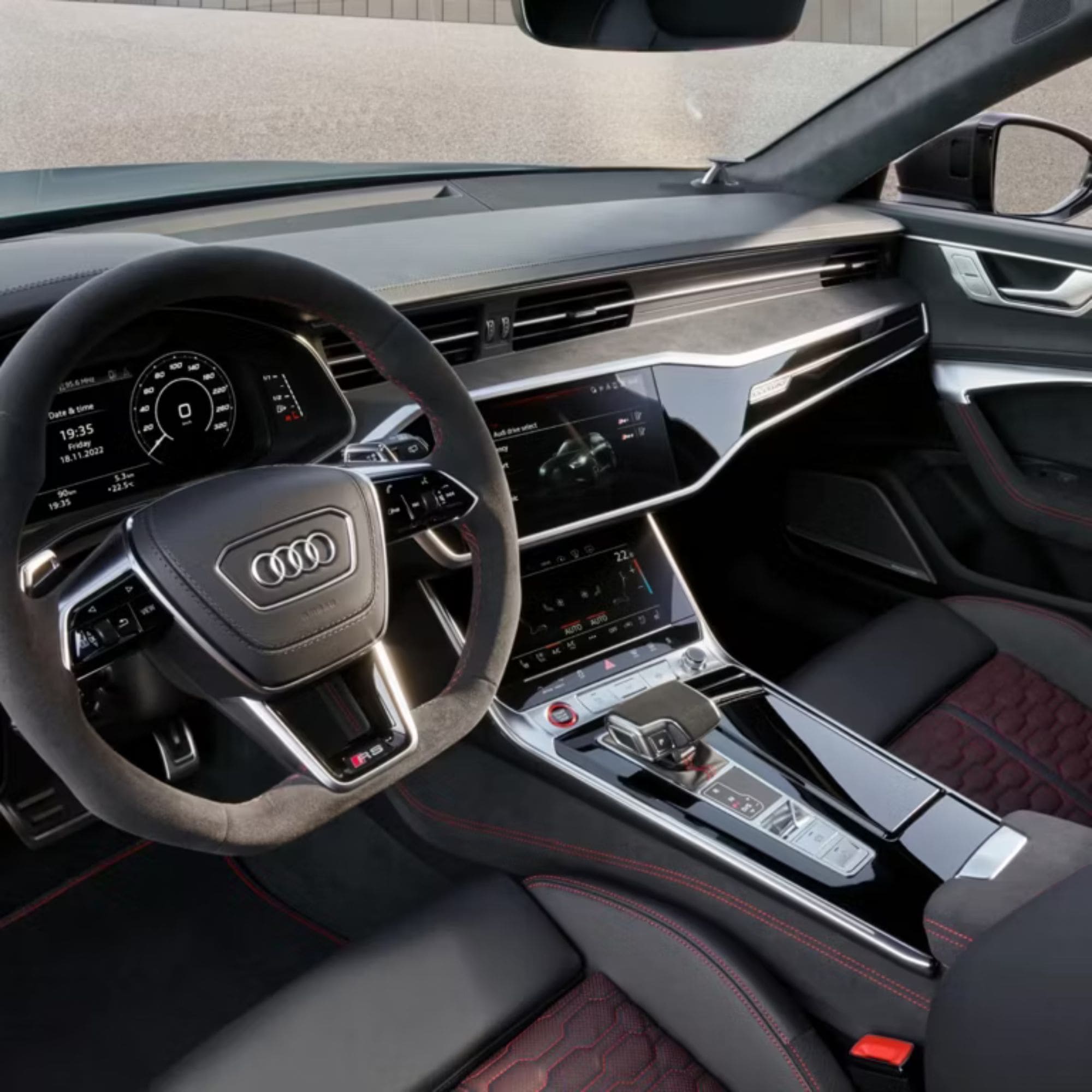 A close-up view of the interior of an Audi car, showing the steering wheel with the Audi logo, the dashboard, the center console, and the seats with black and red stitching.