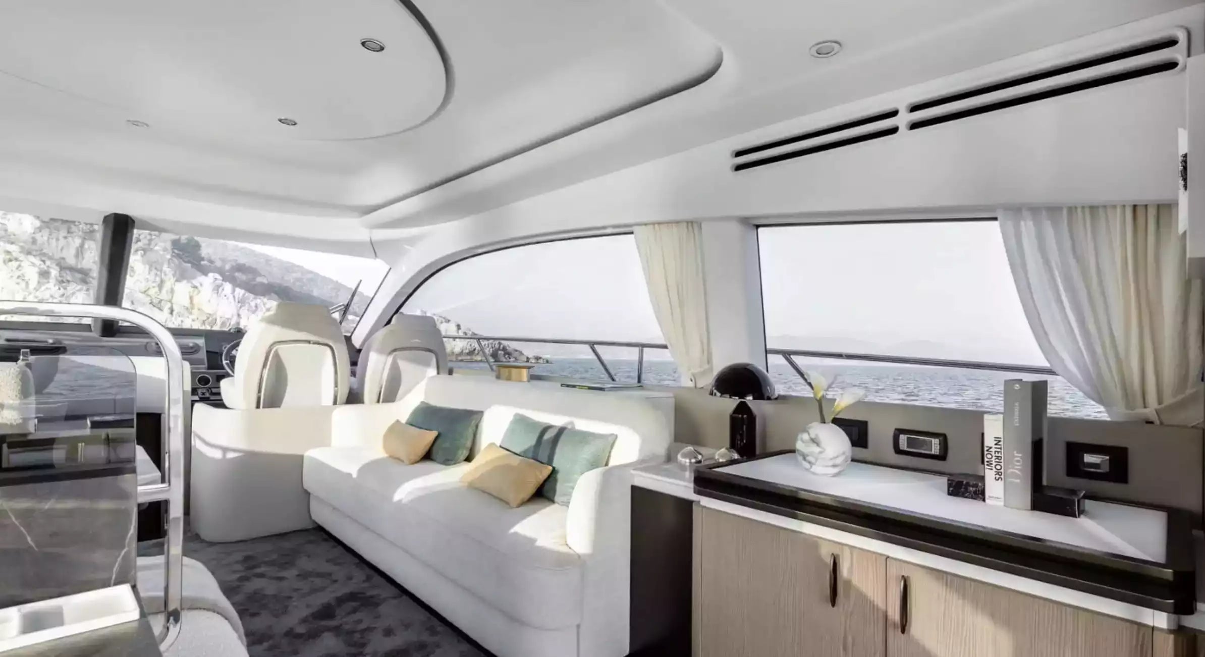 Luxury yacht interior with white sofa, coffee table, and large windows.