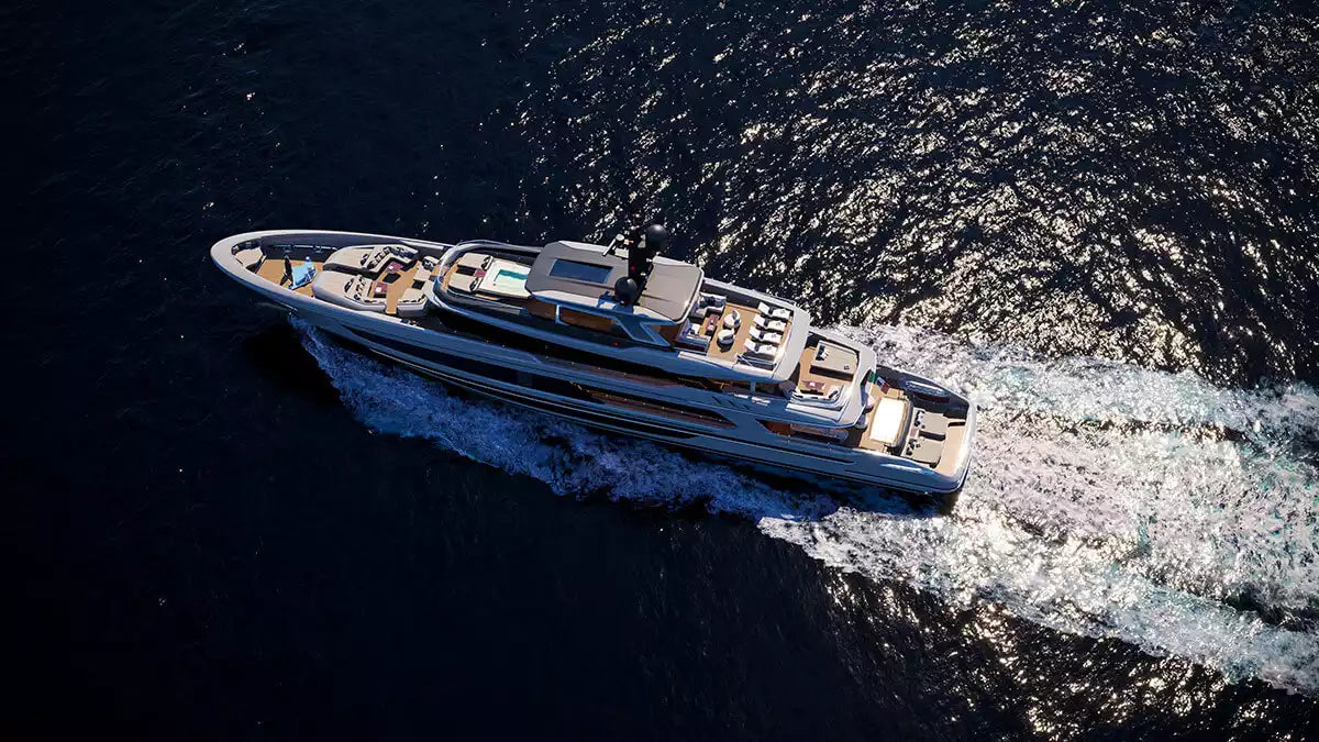 An aerial view of a luxury motor yacht sailing on dark blue water, leaving a white wake behind it.