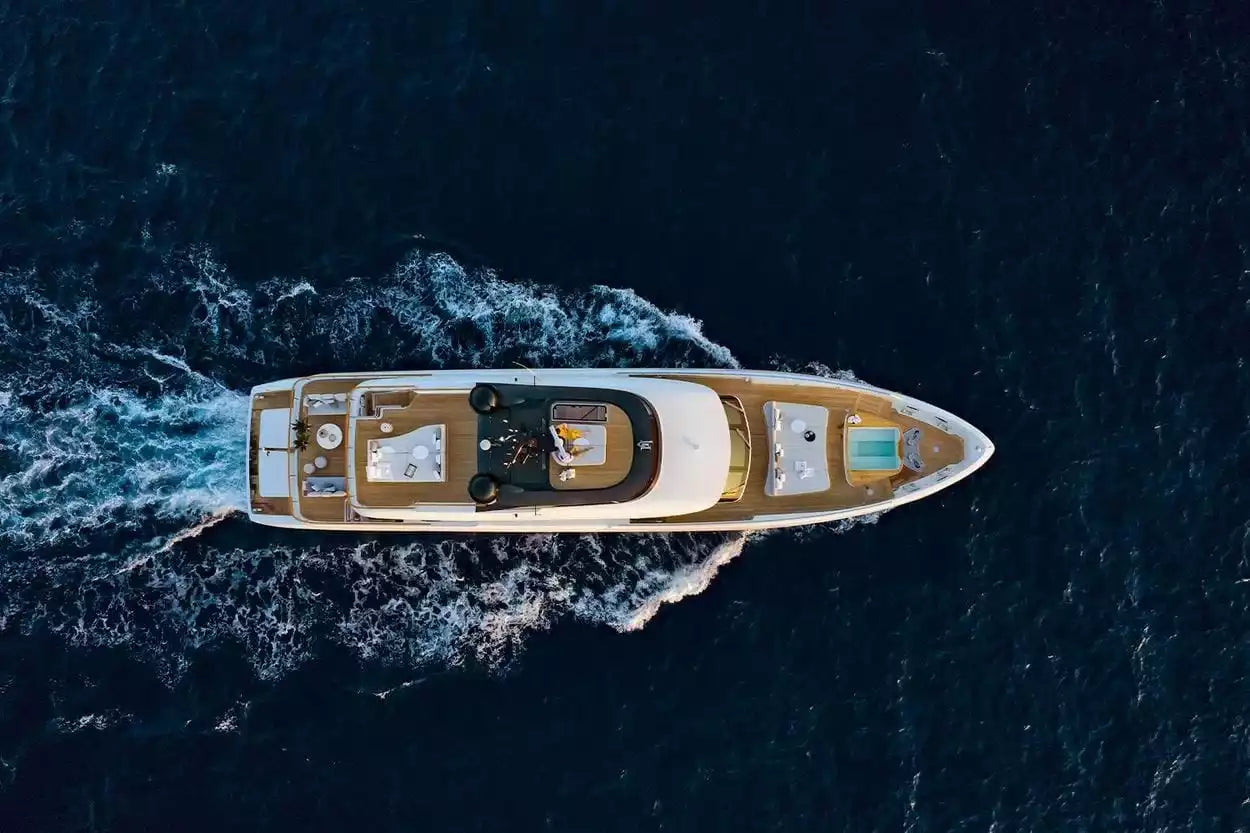 Aerial view of a luxury yacht moving through deep blue ocean water, leaving a white wake behind it.