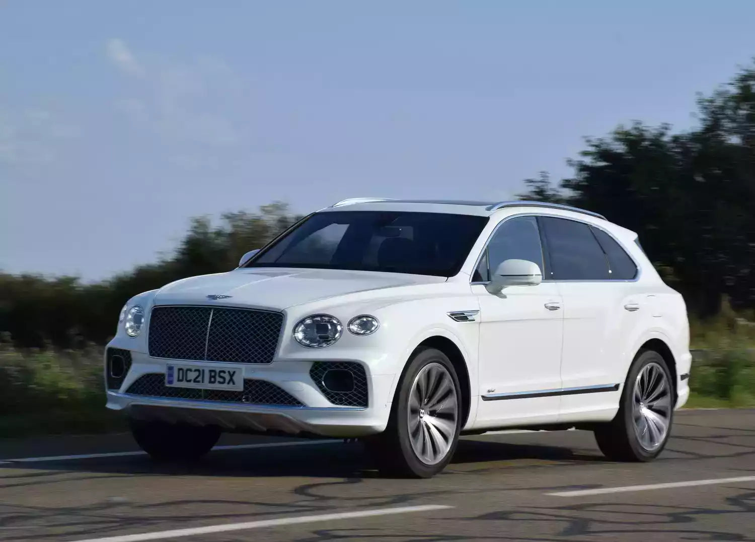 White Bentley SUV driving on a road with trees in the background