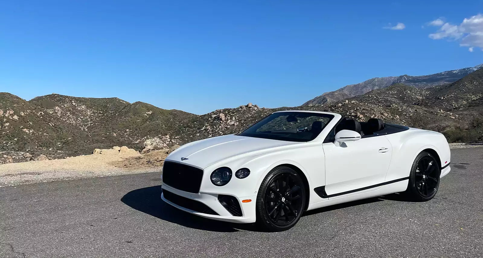White Bentley convertible parked on a road with mountains in the background